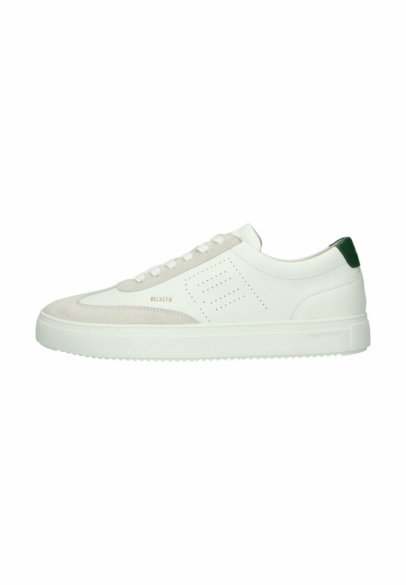 Zapatilla blanca con una puntera de ante y un acento verde en el talón. Diseño perforado en el lateral, cordones planos y suela de goma texturizada.