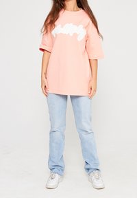 Světle růžové oversized tričko s bílým kurzívním textem, v kombinaci se světle modrými rovnými džíny a bílými teniskami.