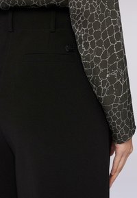 Czarne spodnie o gładkiej fakturze, z tylną kieszenią. Góra ma zielony wzór z jasnoszarymi liniami przypominającymi siatkę.