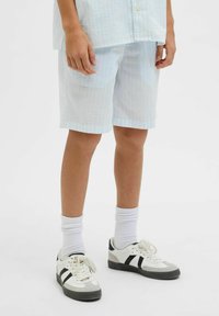 Shorts bleu clair à motif en tissu texturé, associés à des chaussettes blanches et des baskets avec des accents noirs et des détails gris.