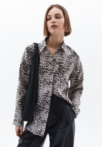 Hedvábná košile s leopardím potiskem v béžové a hnědé barvě, dlouhé rukávy, límeček, zapínání na knoflíky, spárovaná s černými kalhotami a černou kabelkou na rameno.