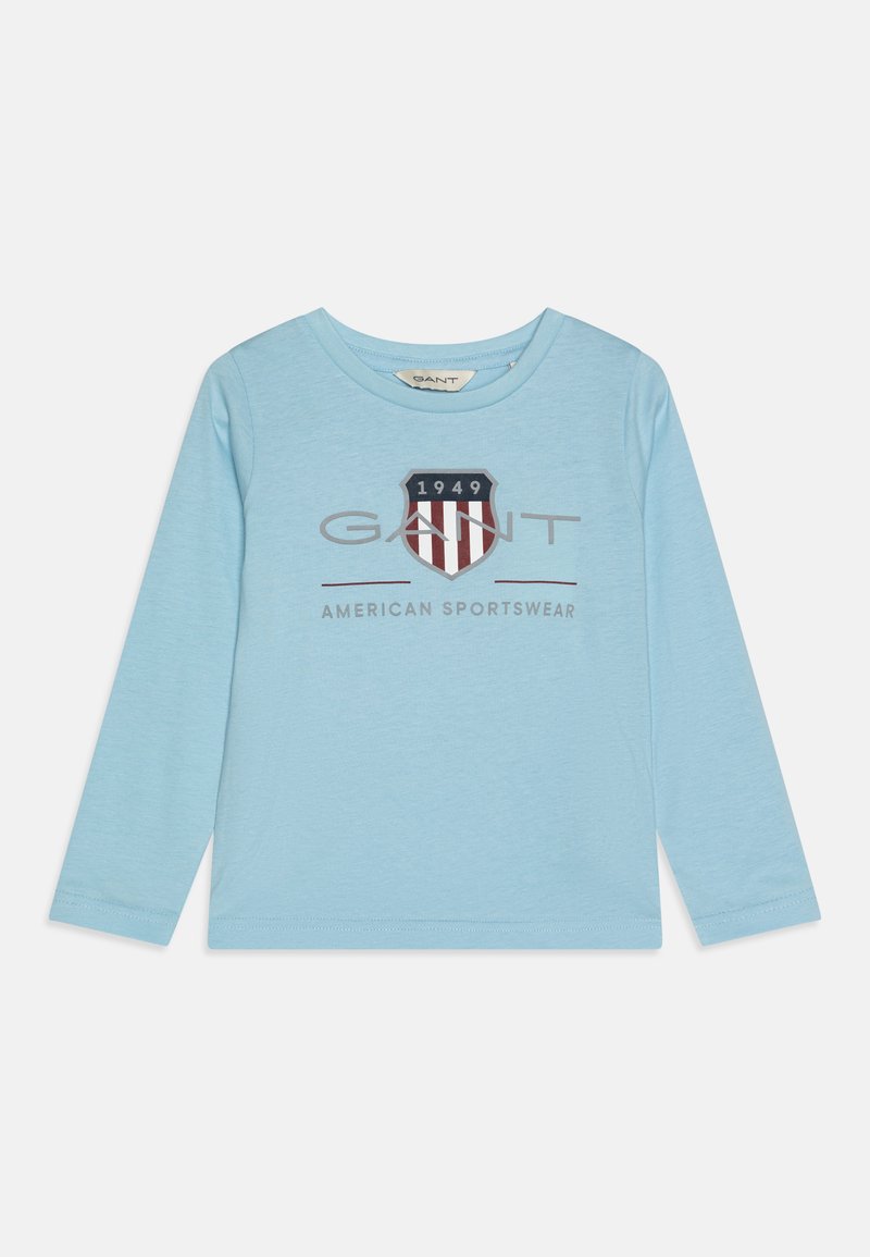 Lyseblå langermet T-skjorte laget av myk stoff, med teksten "GANT AMERICAN SPORTSWEAR" og et skjoldlogo med røde og marineblå striper.