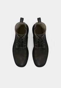 Botines de cuero negro con acabado texturizado, punta redonda y cierre de cordones en la parte delantera. Incluyen una lengüeta para tirar en la parte trasera y un forro interior liso.