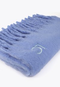 Lys blå uld tæppe med teksturerede frynser i den ene kant og et lille broderet nummer 5 i lys grøn. Blødt og hyggeligt udseende.