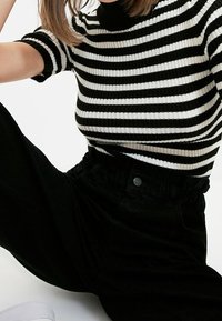 Top rayé noir et blanc à côtes avec des manches courtes, associé à un pantalon noir taille haute avec un détail de bouton et une ceinture élastique.