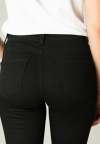 Zwarte spijkerbroek van denim met een aansluitend ontwerp, met een middelhoge taille, achterzakken en een gladde textuur. Geen zichtbare versieringen.