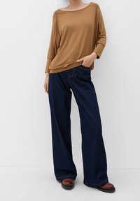 Brązowa bluzka z długim rękawem i szerokim dekoltem, zestawiona z ciemnoniebieskimi, szerokimi dżinsami; obie części wykonane są z miękkiej tkaniny i mają minimalne detale projektowe.