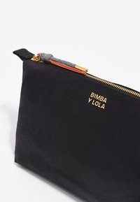 Czarna tkaninowa saszetka z złotym logo "BIMBA Y LOLA", z złotym zamkiem błyskawicznym oraz intensywnymi pomarańczowymi i szarymi akcentami przy uchwycie zamka.