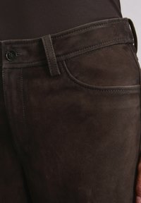 Braune Wildlederhosen mit glatter Textur, ausgestattet mit einer Vorderentasche, Knopfverschluss, genähten Details und einem schmalen Schnitt.