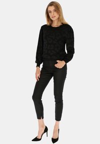 Czarny sweter z subtelnym wzorem, szerokie rękawy, w zestawieniu z czarnymi dopasowanymi spodniami i czarnymi szpiczastymi szpilkami. Prosty, teksturowany design.