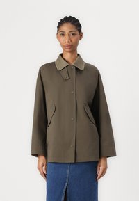 Olivově zelená bunda s měkkým béžovým límcem, patentkami, bočními kapsami a volným střihem. Materiál má hladkou, matnou texturu.