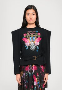 Zwarte longsleeve top met gestructureerde schouders, versierd met kleurrijke bloemen- en vlinderborduursels, en cinched in de taille met een decoratieve riem.
