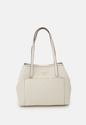 Cremefarbene Guess Tote mit geprägt gestaltetem Logo-Muster, Frontreißverschlusstasche und doppelte Schulterriemen vor einfarbigem Hintergrund.