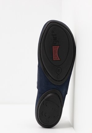 Zapato de ante azul marino con parte superior texturizada y suela de goma negra, que presenta un logotipo impreso y un detalle único en la suela. Talla 38.