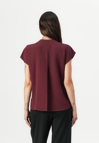 Burgunderfarget kortermet bluse med en avslappet passform, som har rund hals og sentral bakfold, laget av lett materiale.