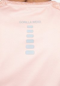 Lichtroze sportshirt met een gestructureerde stof, voorzien van een reflecterende "GORILLA WEAR" logo en een verticale lijn van drie lichtgrijze accenten op de achterkant.