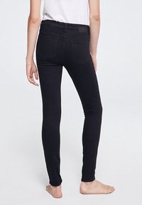 Jean skinny noir avec une texture lisse, taille mi-haute et deux poches arrière. Le design est ajusté et présente des coutures discrètes.