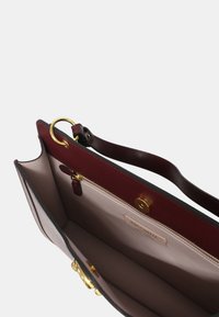 Borsa a mano in pelle borgogna con accentuazione di anello dorato, tasca con zip e fodera interna beige. Presenta una maniglia robusta e un design strutturato.