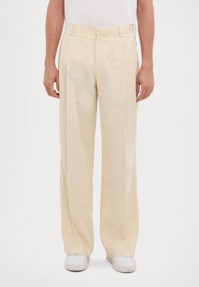 Light beige wide-leg trousers made of smooth fabric, featuring a flat front, front pockets, and tailored waistband, paired with white sneakers.