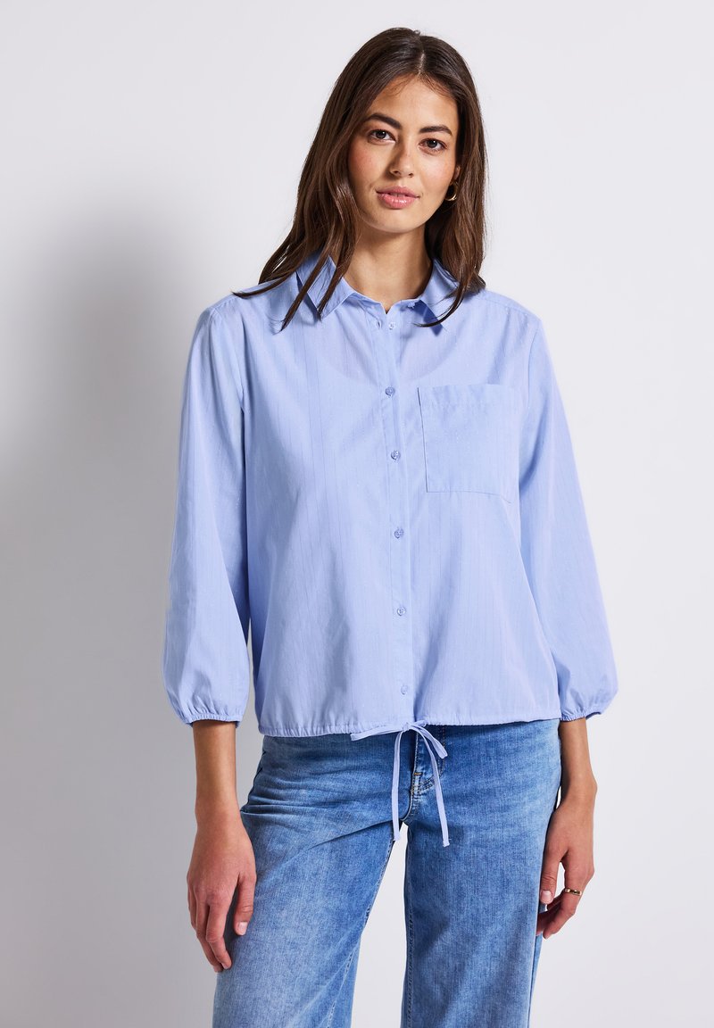 Camicia a maniche lunghe blu chiaro con bottoni, dotata di tasca e orlo con coulisse. Realizzata in tessuto liscio con strisce verticali testurizzate.