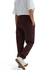 Bordeaux sweatpants met een relaxte fit, een elastische tailleband en cuffed enkels, gecombineerd met witte sneakers met rode accenten.