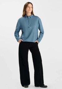 Lichtblauwe denim-look pullover met een kraag en een knoopsluiting aan de voorkant, gecombineerd met zwarte brede broekspijpen. Glad textuur, casual ontwerp.