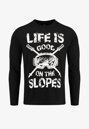 Schwarz langärmliges Shirt mit weißem, abgenutztem Text "DAS LEBEN IST GUT AUF DEN PISTEN" sowie einer Illustration von Skibrillen und gekreuzten Skistöcken.