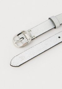 Sidabrinė diržo, pagaminto iš dirbtinės odos, paviršius yra tekstūruotas, su metaline sagtimi ir reguliuojamomis skylutėmis dirže dydžio pritaikymui.