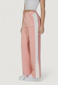 Pantaloni a gamba larga rosa con strisce laterali bianche e dettagli con bottoni alle caviglie. Realizzati in un tessuto morbido, con vita elastica e tasche.