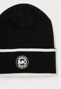 Schwarze gestrickte Mütze mit einem weißen horizontalen Streifen und einem runden Logo-Patch, das die Texte "MK" und "MICHAEL KORS" enthält.