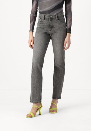 High-waisted gray jeans with a textured finish, featuring five pockets and a belt loop. Paired with bright yellow strappy heels.