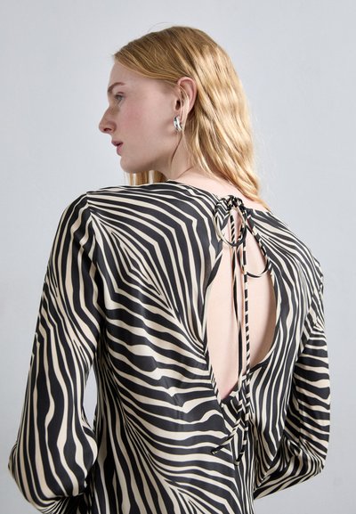 Long-sleeve, backless dress in black and cream zebra stripes. Features a tie closure and round accents at the neckline. Silky texture.