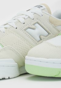 Détail de la basket New Balance 550 blanc cassé montrant des textures en daim et mesh, des lacets blancs et un bord de semelle vert clair.