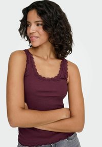 Bordeauxkleurige geribbelde tanktop met kanten randje bij de halslijn en bandjes. Heeft een geschulpt zoom en een aansluitend model.