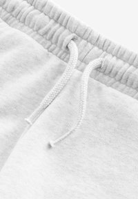 Pantalons de survêtement gris clair avec une taille élastique, cordon de serrage et texture douce. Couture visible et subtils détails de grain de tissu.