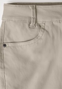 Beige stoffen broek met een tailleband met riemlussen, een voorzak met een metalen klinknagel en zichtbare stikseldetails.
