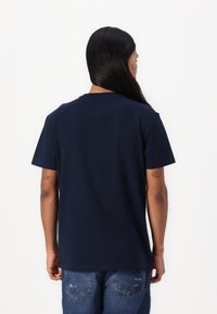 Navyblauwe katoenen T-shirt met een klassieke ronde hals, korte mouwen en een losse pasvorm, gecombineerd met denim jeans met zichtbare stiksels.
