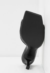 Zapato de tacón alto negro con punta cuadrada y parte superior de cuero texturizado. Presenta una suela negra lisa y un tacón bajo. Talla 37.