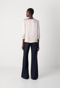 Light pink silk blouse with three-quarter puff sleeves, paired with dark blue wide-leg jeans featuring a curved back pocket detail.