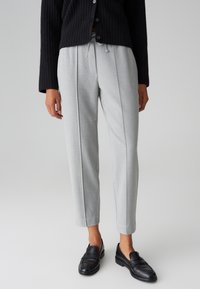 Grau maßgeschneiderte Hose mit lockerer Passform, ausgestattet mit Falten, einem Kordelzugbund und kombiniert mit schwarzen Lederloafern. Strukturierter Strickcardigan.