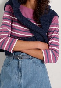 Długim rękawem, w paski w kolorach purpurowym, białym i granatowym, w połączeniu z jasnodenim spódnicą oraz ciemnoniebieskim swetrem wełnianym narzuconym na ramionach.