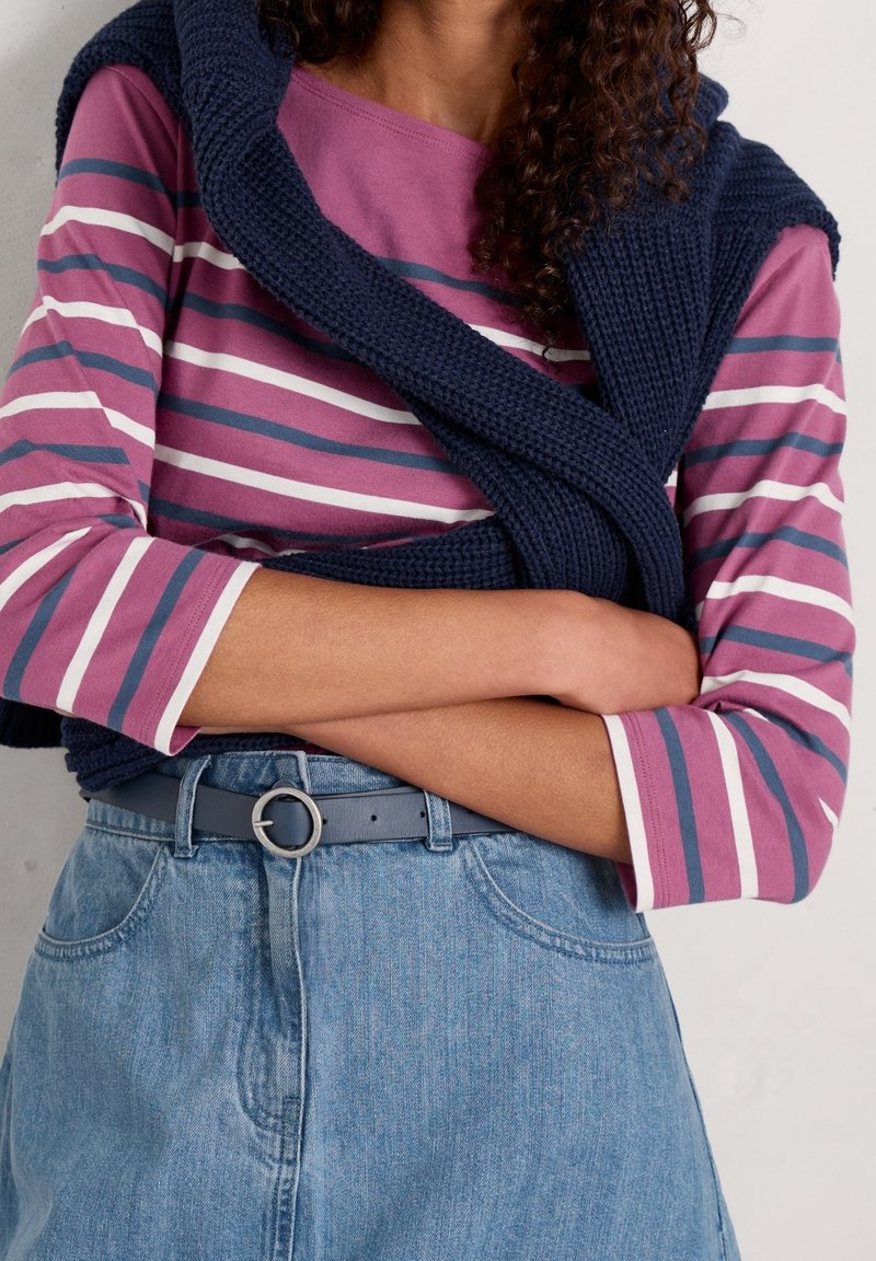 Długim rękawem, w paski w kolorach purpurowym, białym i granatowym, w połączeniu z jasnodenim spódnicą oraz ciemnoniebieskim swetrem wełnianym narzuconym na ramionach.