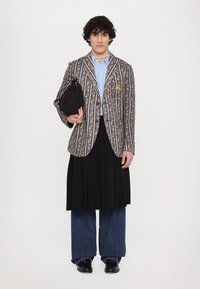 Striped floral blazer with buttons, light blue shirt, black pleated skirt, and wide denim pants. Black bag and smooth black shoes complete the look.