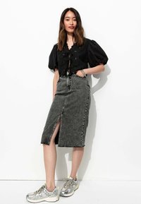 Haut noir à manches bouffantes, jupe en denim près du corps avec une fente sur le devant et un ourlet effiloché, associée à des baskets de sport grises et argentées.