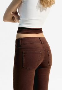 Jeans de denim marrón con un ajuste slim, cintura de altura media y bolsillos traseros. La tela tiene un acabado limpio y un ligero estiramiento para mayor comodidad.