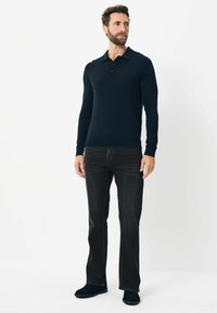 Marineblå langærmet polo shirt med krave og tre knapper, parret med mørke jeans og mørkt fodtøj. Enkel, tætsiddende design.