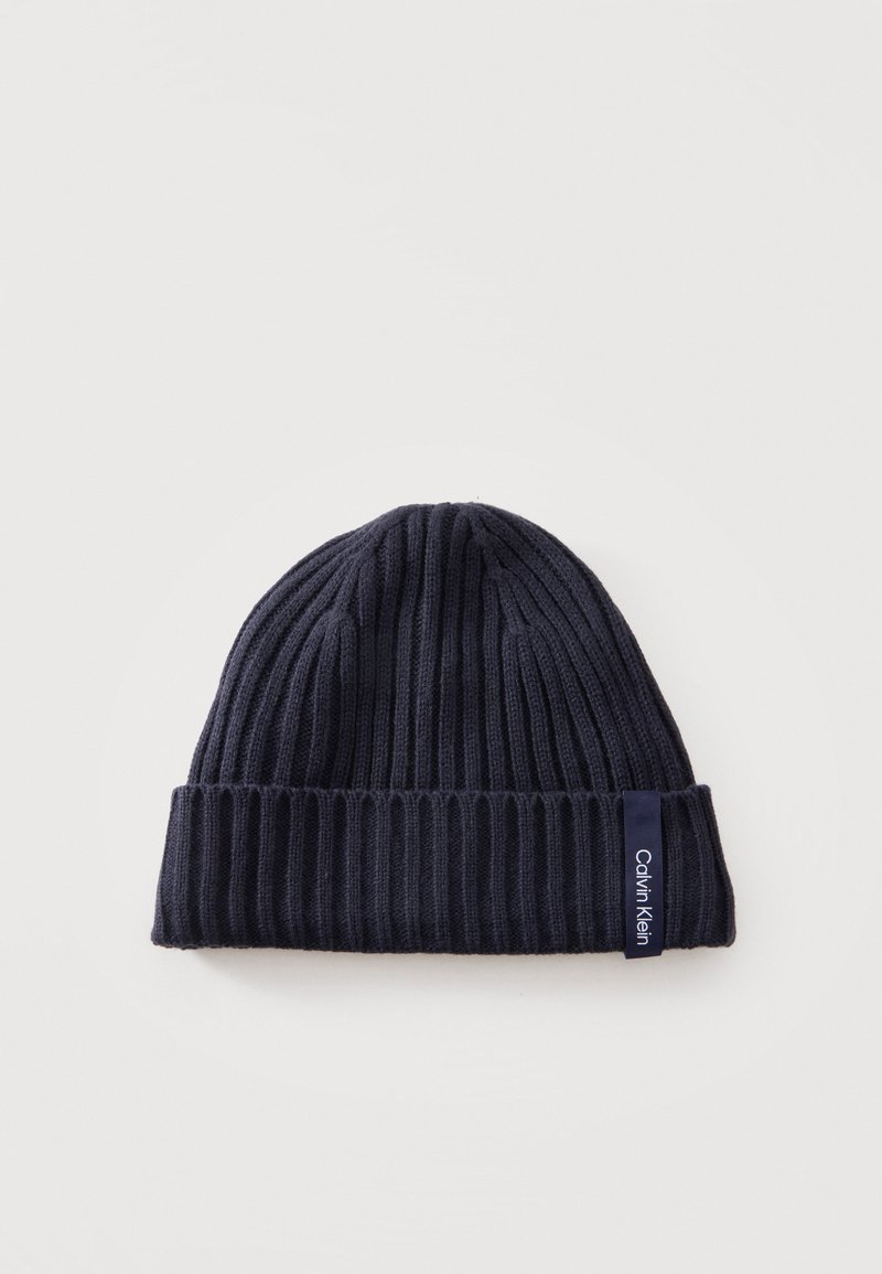 Bonnet en maille côtelée bleu marine foncé avec revers plié et étiquette visible de la marque Calvin Klein sur le bord du revers.