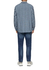 Blauw-wit geruite langermige shirt met kraag, gecombineerd met donkerblauwe jeans en lichtgekleurde sneakers, gezien vanuit de achterkant.