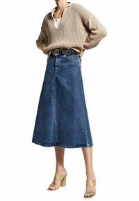 Béžový pletený svetr s V výstřihem, nošený přes bílý top. Tmavě modrá denimová sukňa ve tvaru A s předním švem a černým páskem. Sandály se zlatými pásky.