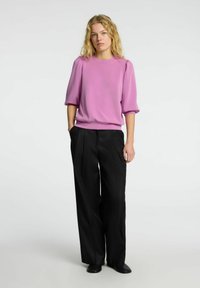 Top corto a maniche corte rosa e texturizzato con dettaglio arricciato sulle spalle, abbinato a pantaloni neri a vita alta e larghi e scarpe nere.